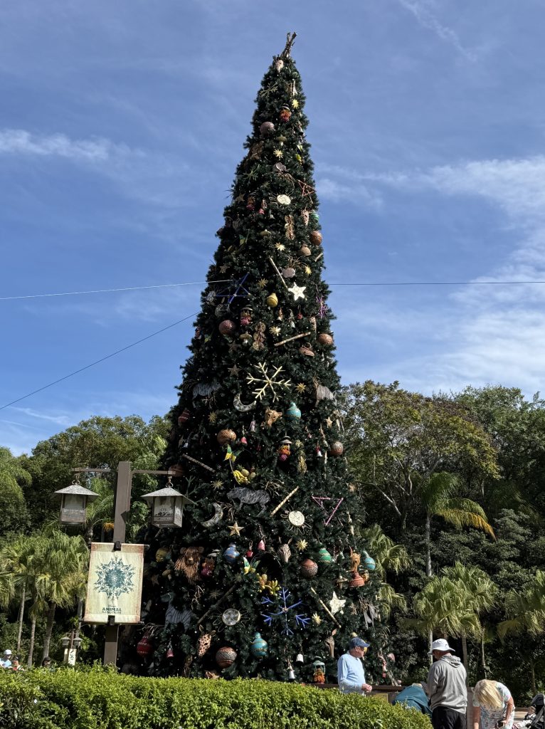 A tall, decorated Christmas tree adorned with colorful ornaments and festive decorations, surrounded by greenery and people enjoying the holiday atmosphere.